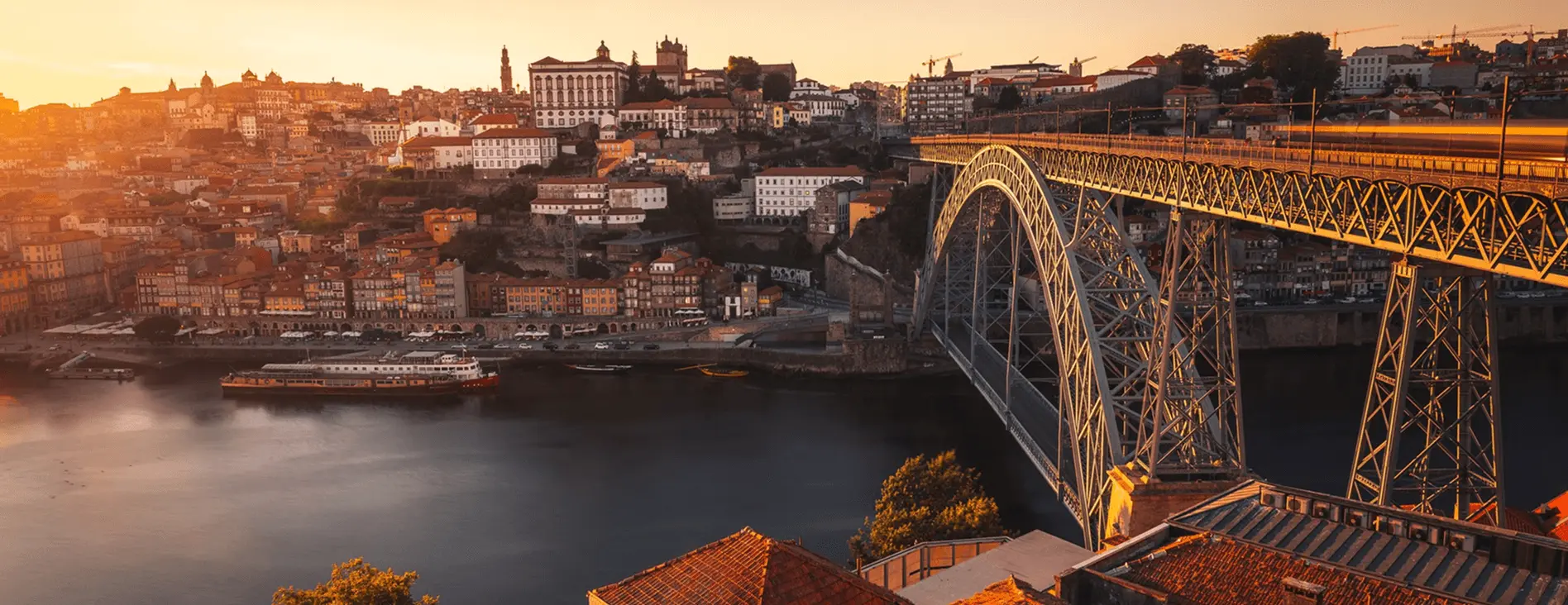 Vista panorâmica do Porto ao pôr do sol, com a Ponte Dom Luís I em destaque sobre o Rio Douro e o centro histórico da cidade ao fundo, em Portugal.