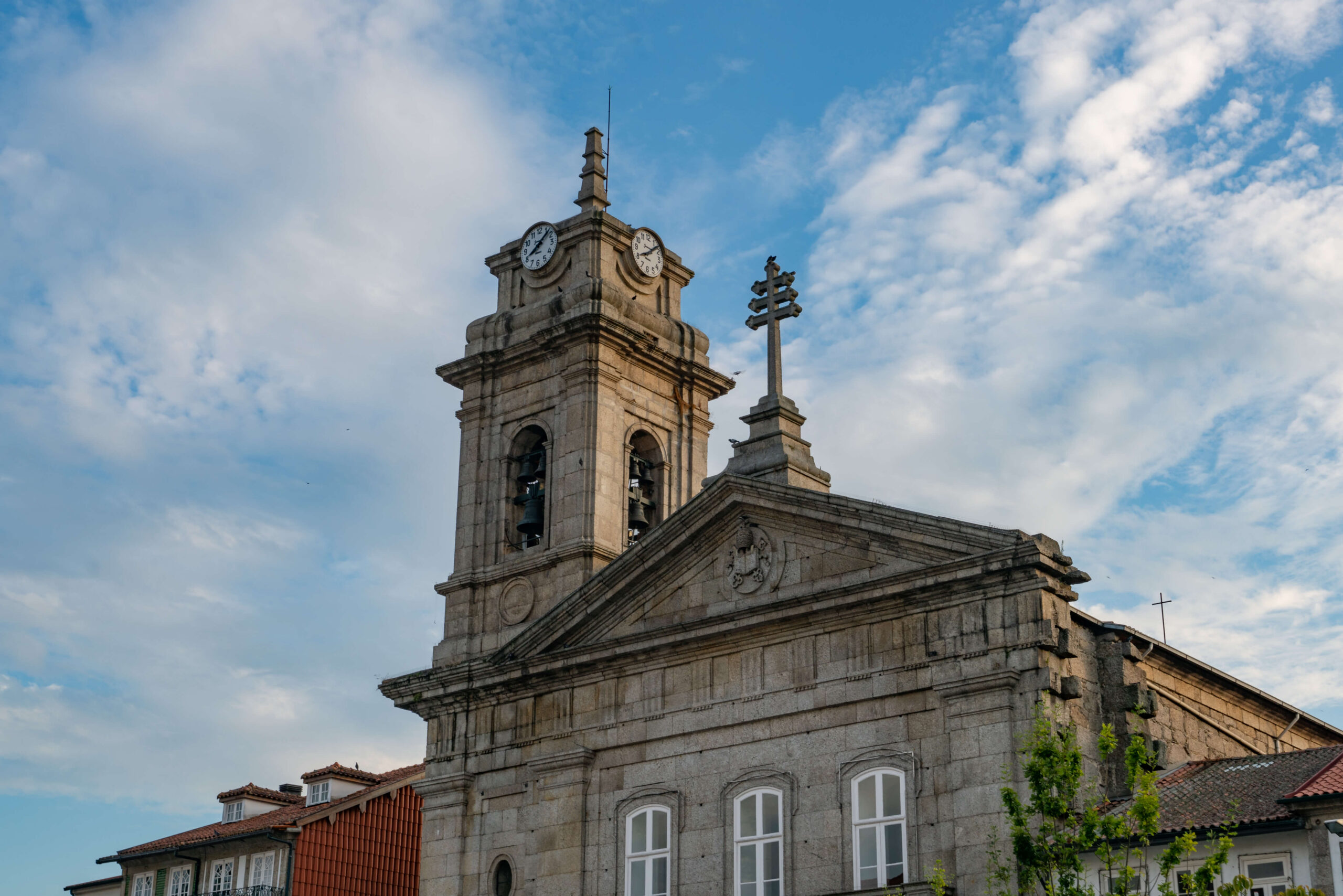 Fachada barroca do Santuário do Bom Jesus do Monte em Braga, com duas torres sineiras, escadaria monumental com estátuas e fonte, jardins floridos e vegetação exuberante ao fundo, em Portugal.